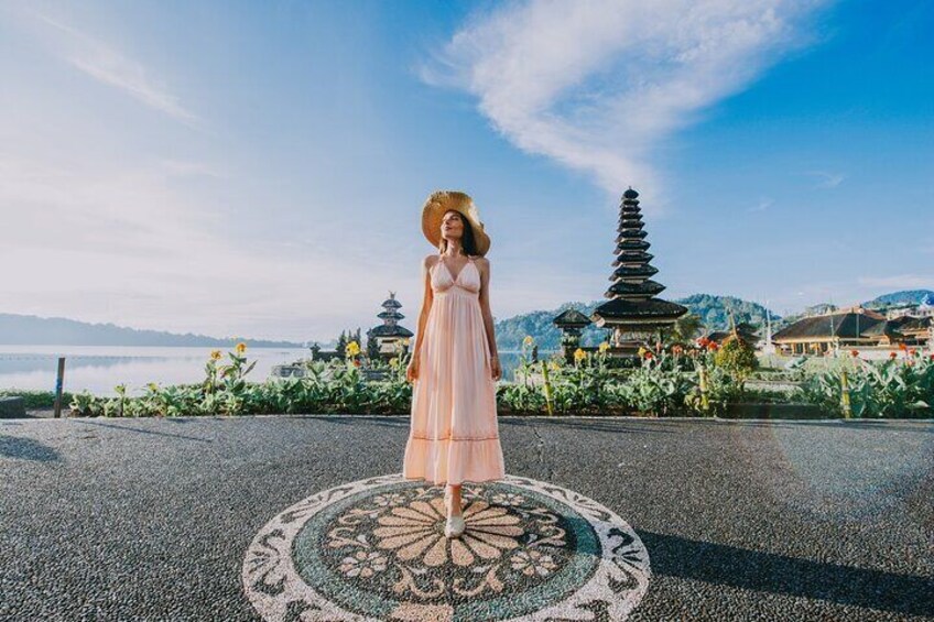 A person in a dress standing on a patterned mat with a pagoda and mountains in the background. 5