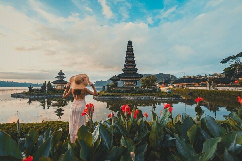 A person in a white dress and straw hat standing by a pond with lotus flowers, looking at pagodas and a temple in the background. 4