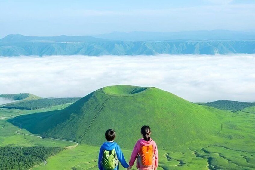 Two people hiking on a green mountain with a valley and clouds below. 4
