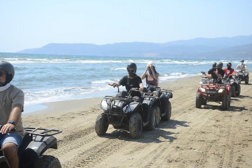 A group of people on ATVs on a sandy beach with the ocean and mountains in the background. 3