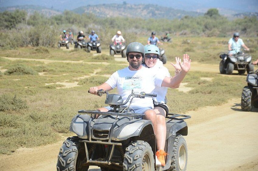A person riding an ATV on a dirt road with other ATVs in the background. 2