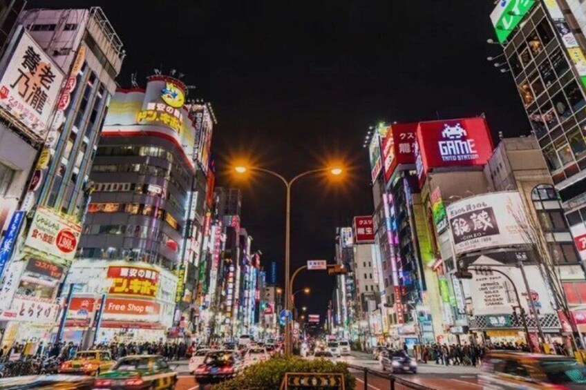 A brightly lit urban street at night with illuminated billboards and signs. 5