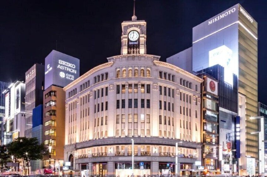 A historic building with a clock tower, surrounded by modern skyscrapers and illuminated signs. 4