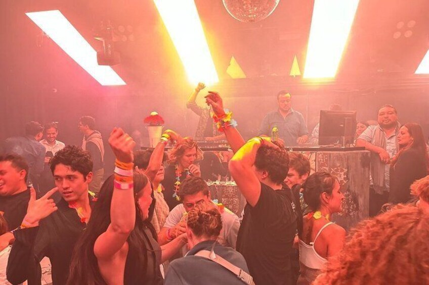 A crowded indoor event with people dancing and a DJ booth in the background. 2