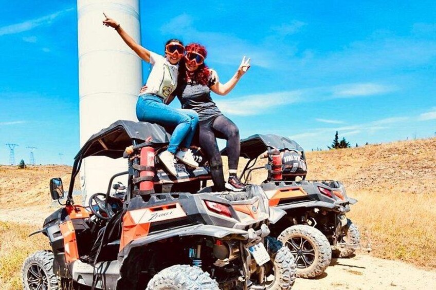 Two people on a quad bike with a large cylindrical structure in the background. 4