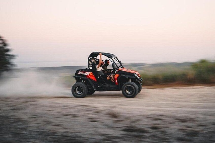 A person driving a black and red ATV on a dirt road with a dust trail behind. 5