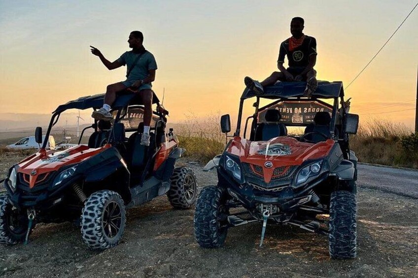 Two off-road vehicles parked on a dirt road with a sunset in the background. 3