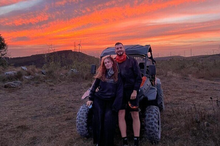 A sunset with a couple on a quad bike in a grassy field. 2