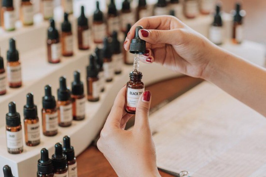A person holding a small bottle with a dropper, surrounded by various bottles on shelves. 2