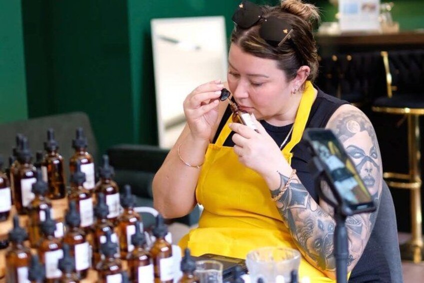 A person in a yellow apron holding a pen, surrounded by bottles. 1