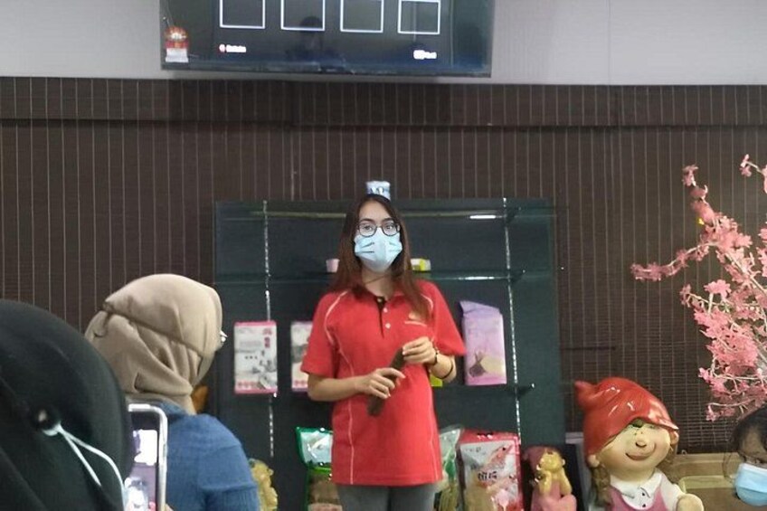 A person in a red shirt holding a microphone, standing in front of a display with various items and a decorative tree. 2