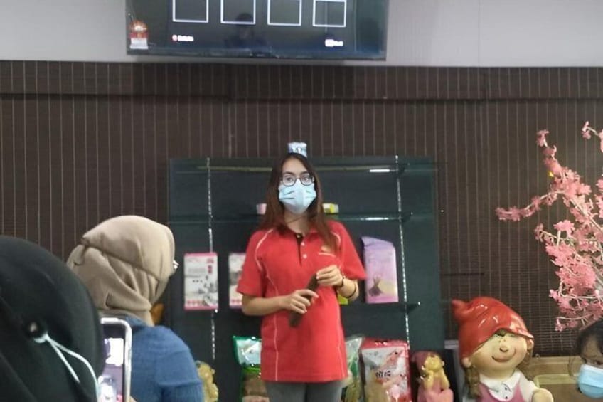 A person in a red shirt holding a microphone, standing in front of a display with various items and a decorative pink tree. 2