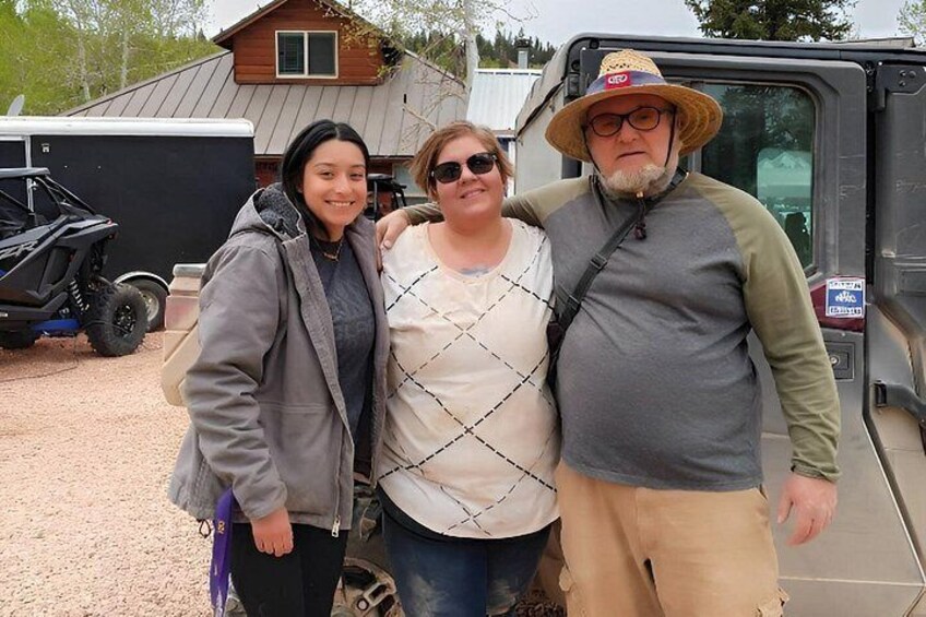 Three people standing in front of a vehicle, a trailer, and a house with a metal roof. 5