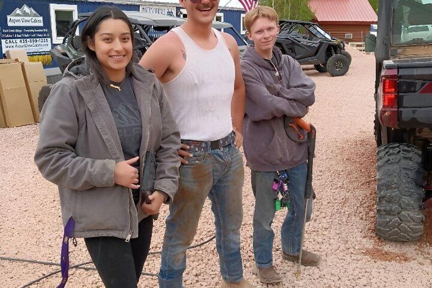 Three people standing in front of a vehicle on a gravel surface. 4