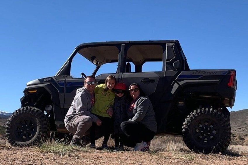 A group of people posing with a black off-road vehicle in a natural landscape. 3