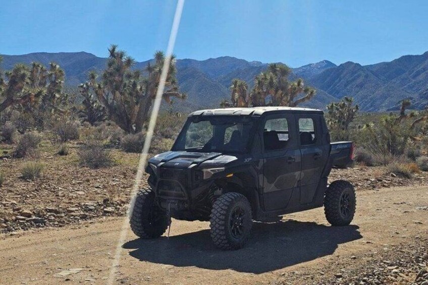A black off-road vehicle parked on a dirt road with desert vegetation and mountains in the background. 1