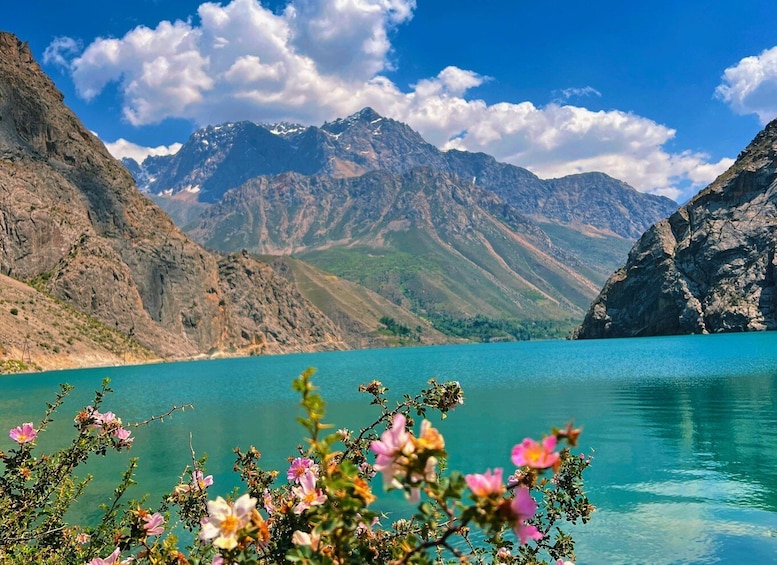 A mountain lake with clear turquoise water, surrounded by rugged mountains and blooming pink flowers in the foreground. 3