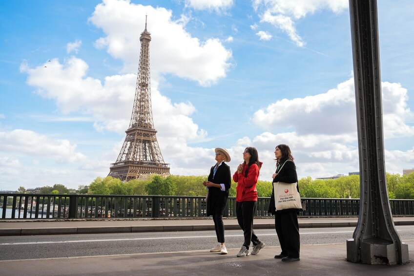 Taustalla näkyy Eiffel-torni, edessä sillan kaide ja punatakkinen henkilö. 1