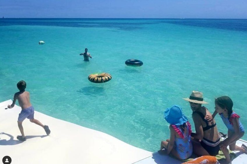 A beach scene with clear turquoise water, a person swimming, and a child playing with a ring. 1