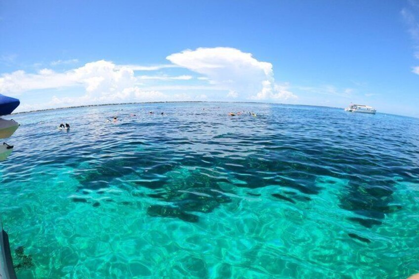 A clear blue sea with people swimming and a boat in the distance. 3