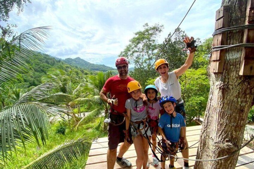 A group of people on a zip-lining course with lush greenery and trees in the background. 1