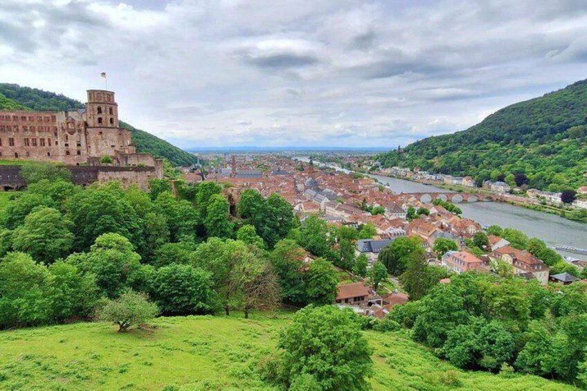Een historisch kasteel met uitzicht op een rivier, omgeven door weelderige begroeiing en een stad. 2
