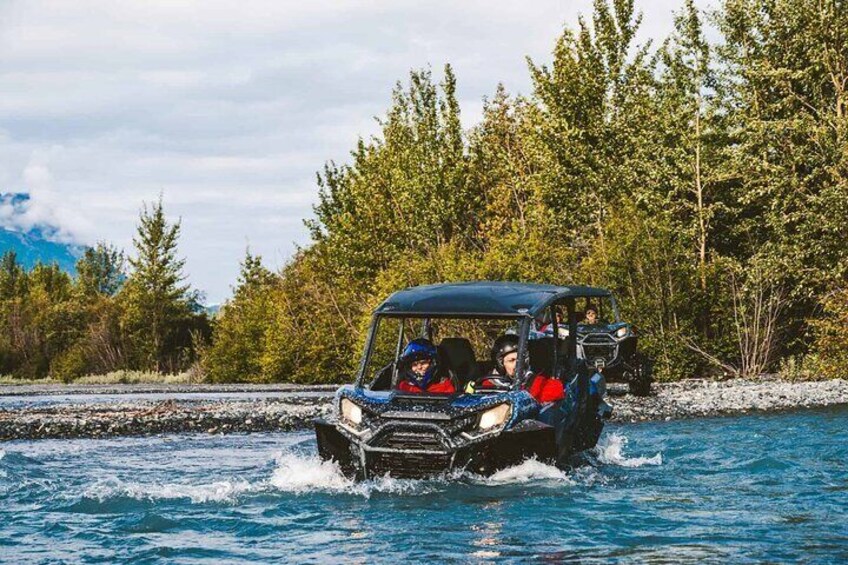 A vehicle driving through a river surrounded by trees. 1