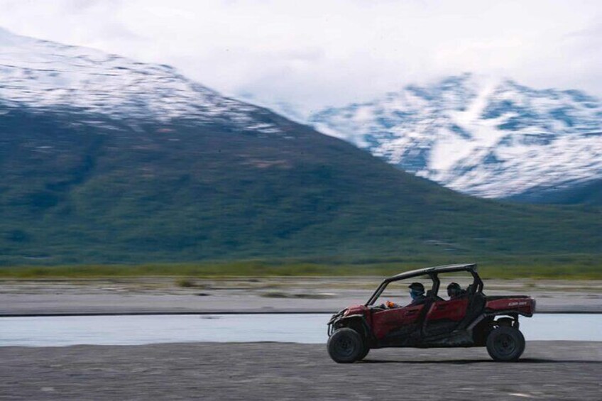 A red off-road vehicle on a paved surface with a mountainous landscape in the background. 5