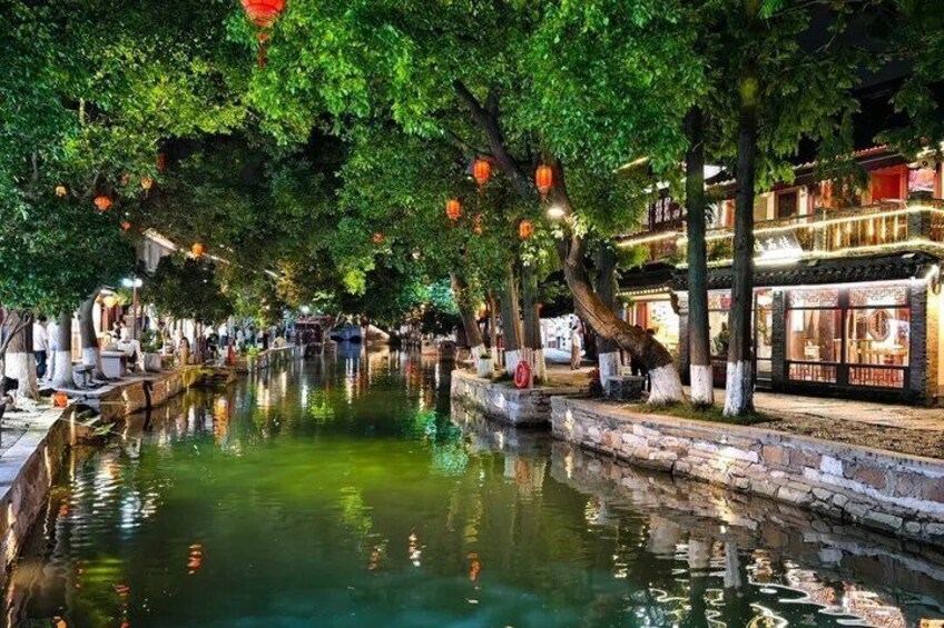 A canal lined with trees and traditional buildings, illuminated by lanterns. 1