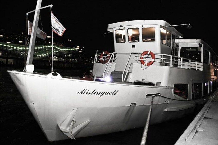 A white boat named 'Mistingell' docked at night with city lights in the background. 4