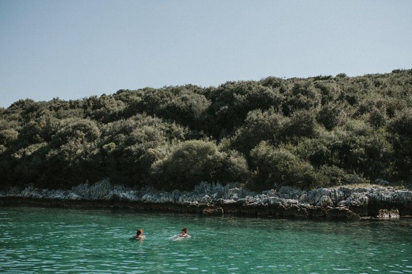 A calm body of water with two people swimming, surrounded by dense green foliage and a rocky shoreline. 4