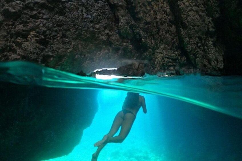 A person swimming underwater in a clear blue pool with rocky walls. 5
