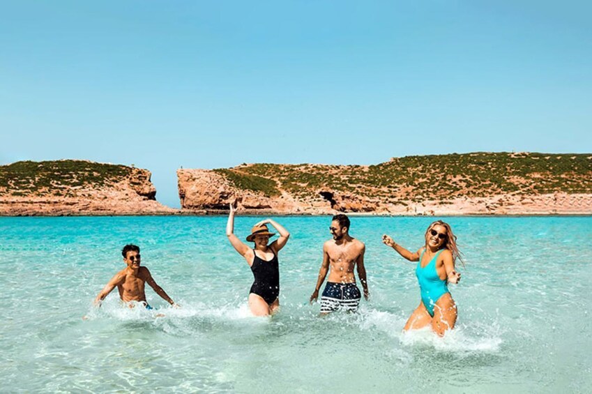Four people in a clear blue sea with rocky cliffs in the background. 1