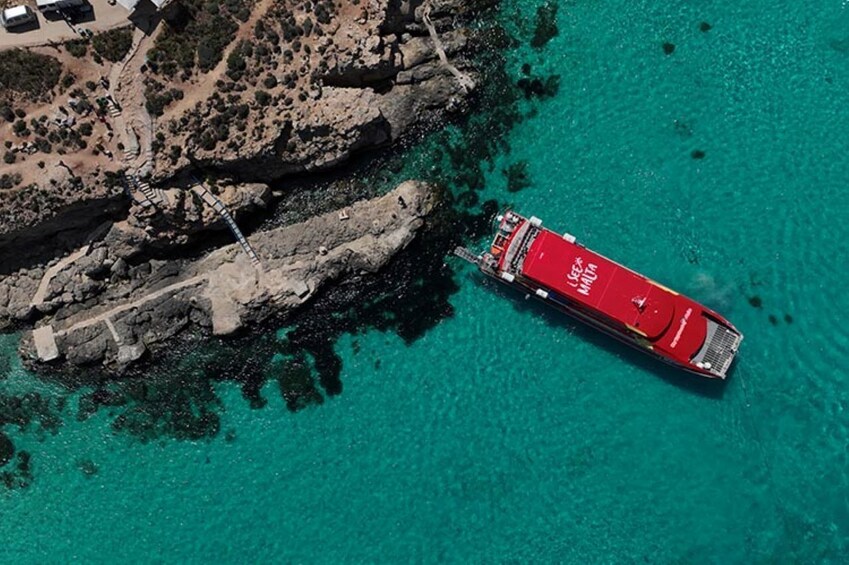 A red ship docked at a rocky coastline with clear turquoise water. 5