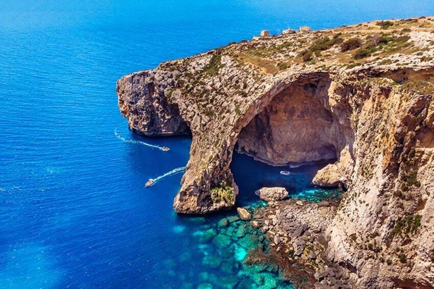 A coastal cliff with a natural arch formation and clear blue waters. 3