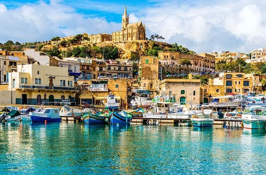 Un pueblo costero con una iglesia destacada en una colina, barcos amarrados en el puerto y una combinación de edificios tradicionales y modernos. 2