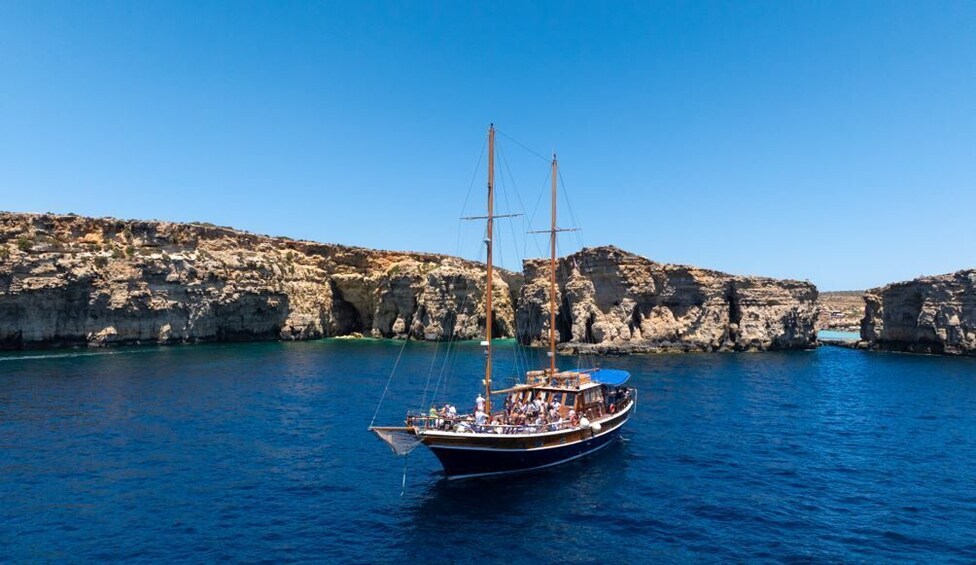 A sailing boat on calm blue waters with rocky cliffs in the background. 4