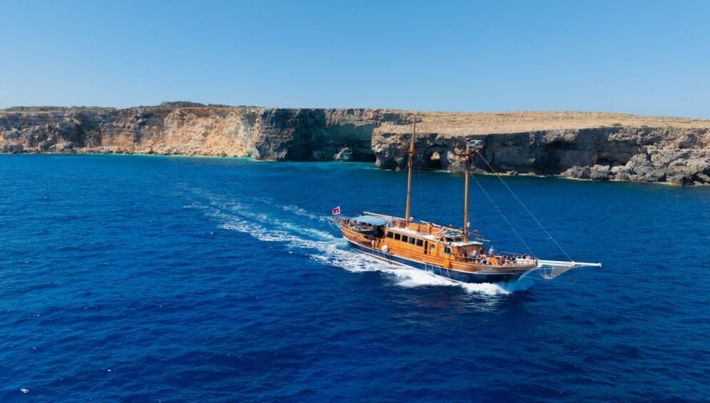 A wooden boat sailing on a blue sea with rocky cliffs in the background. 2