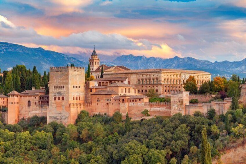 A historic fortress with a prominent tower, surrounded by lush greenery and mountains in the background. 1