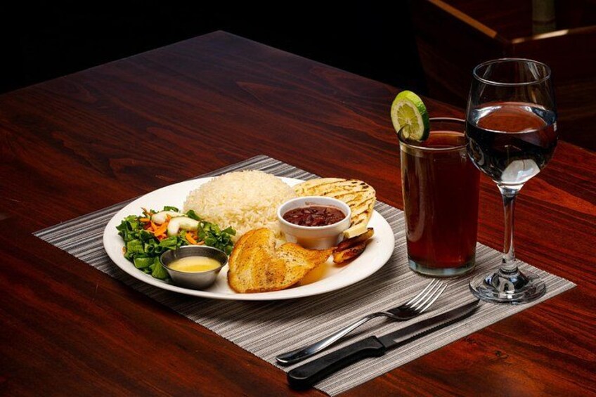 A plate of food with rice, salad, and a fried item, accompanied by a glass of iced tea and a glass of red wine. 3