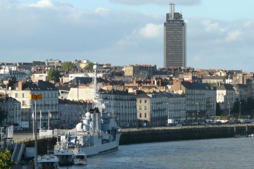 A large naval ship docked at a harbor with a cityscape in the background. 3