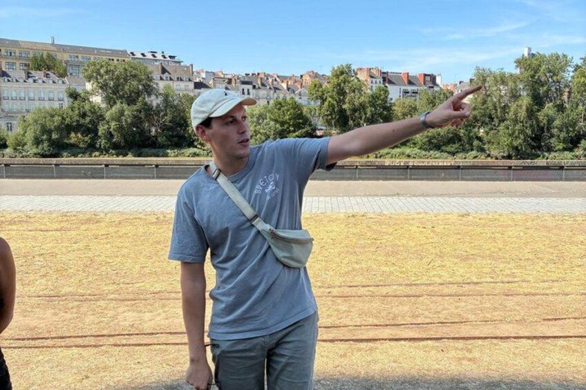A person pointing towards the horizon in an open field with buildings in the background. 3