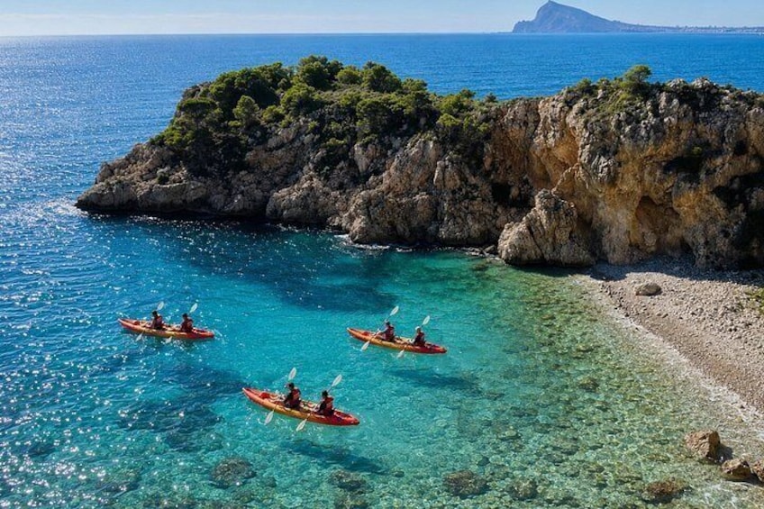 Kayakers on a clear blue sea, rocky coastline, and a distant island. 5