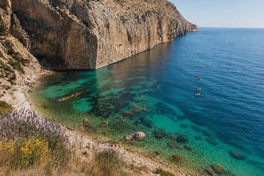 A coastal landscape with clear blue waters, rocky cliffs, and sparse vegetation. 4
