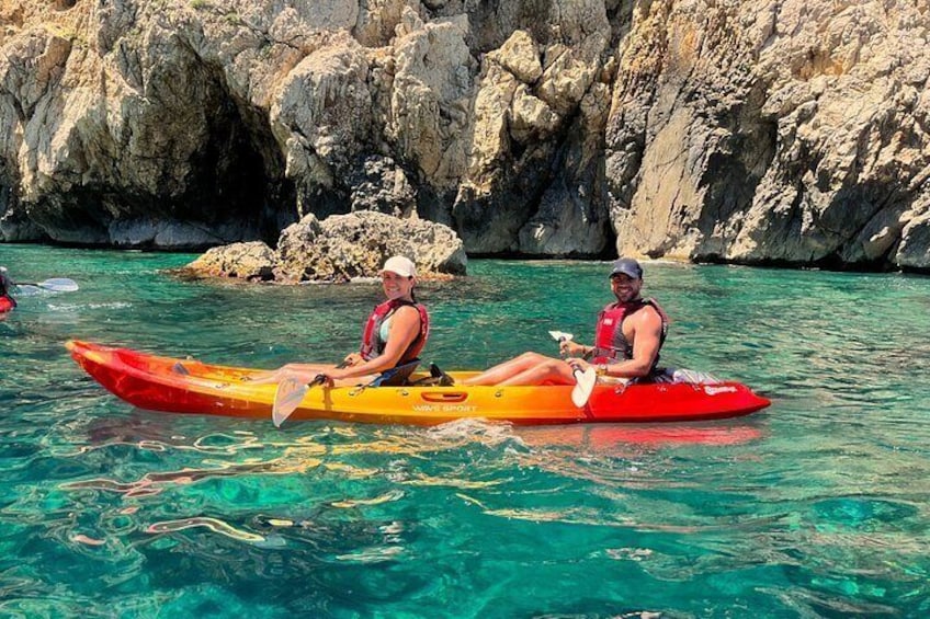 Two people kayaking on clear turquoise water with rocky cliffs in the background. 2