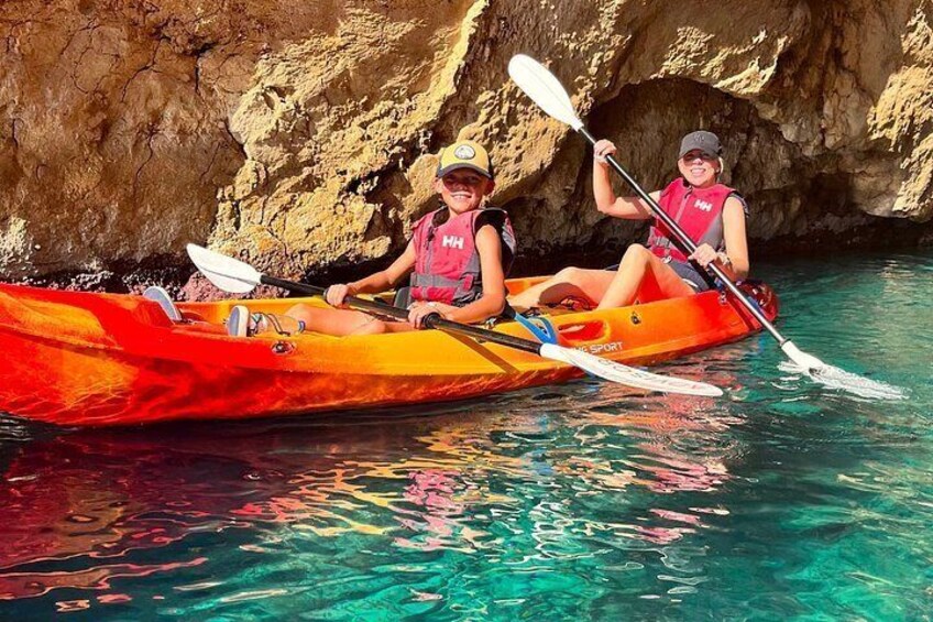 Two people kayaking in a red kayak on clear water with a rocky background. 3
