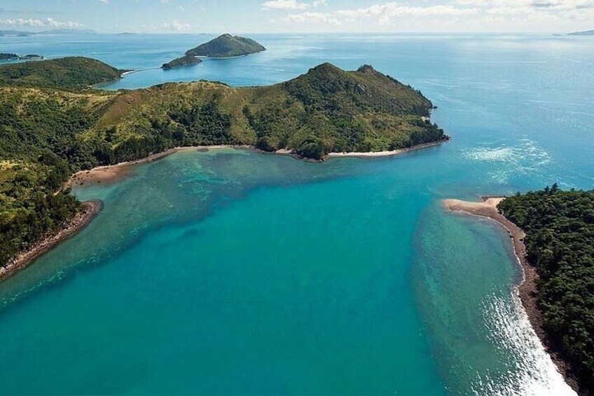 A coastal landscape with clear turquoise waters, sandy beaches, and lush green hills. 2