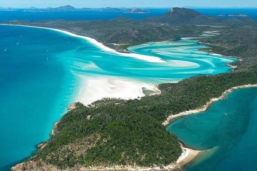 A coastal landscape with turquoise waters, sandy beaches, and dense green forests. 5