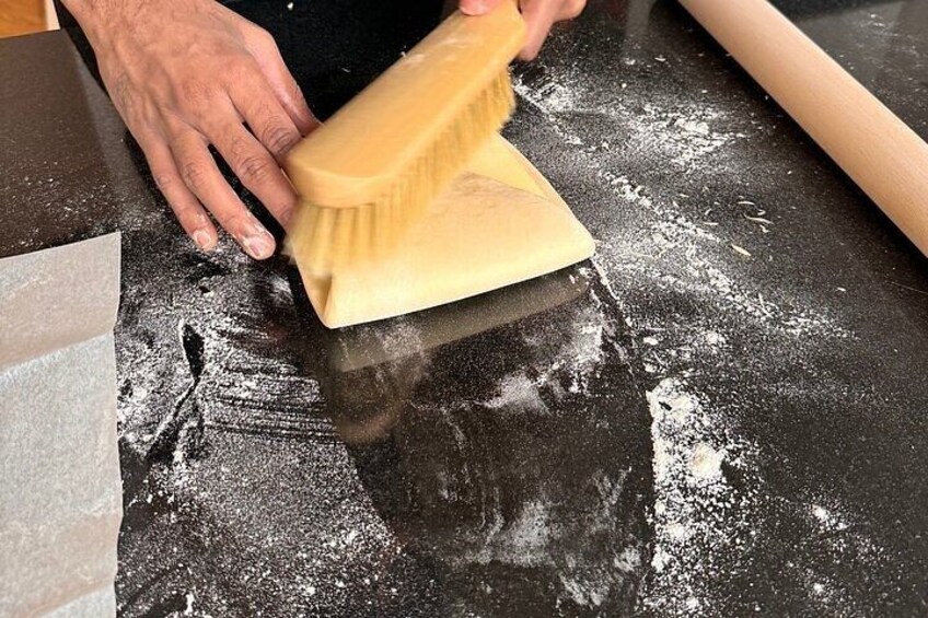 A person using a wooden brush to clean a black surface with flour. 3