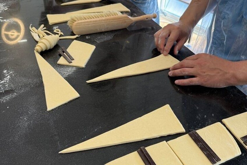 A person preparing dough on a black countertop with various tools and shapes of dough. 4